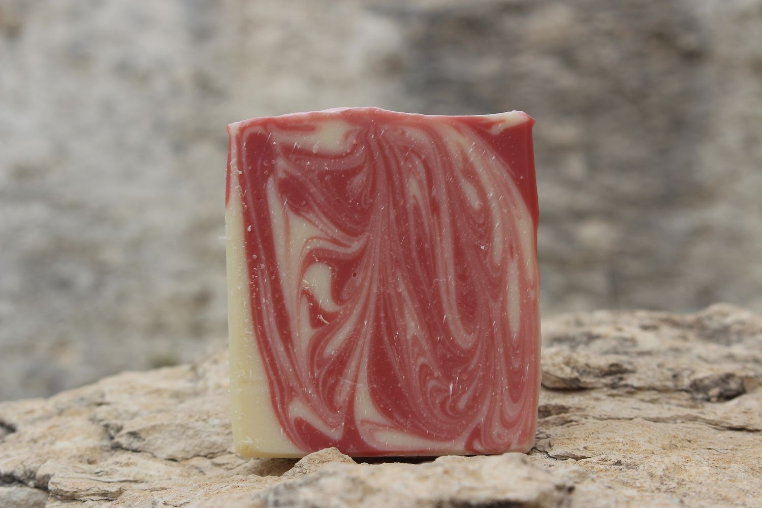 Marbled red and white soap bar on a stone surface with a blurred natural background